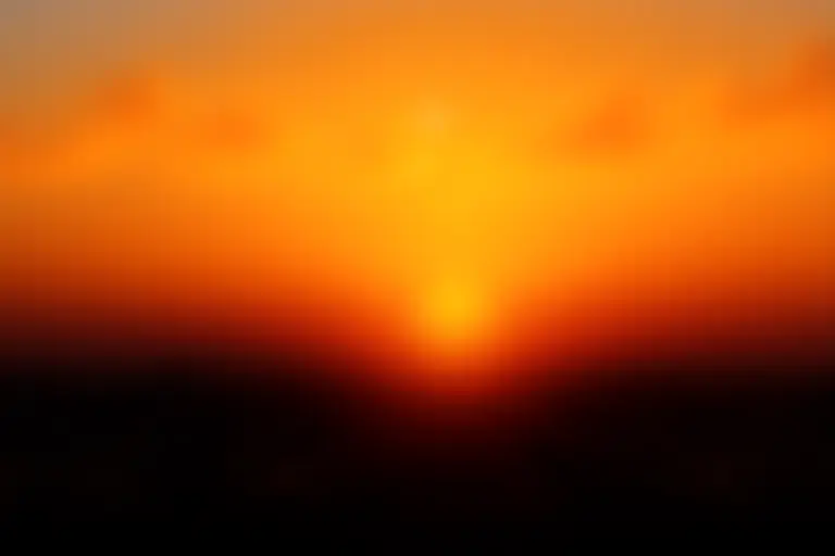 An elderly person sitting peacefully on a bench overlooking a sunset with an expression of quiet resolve