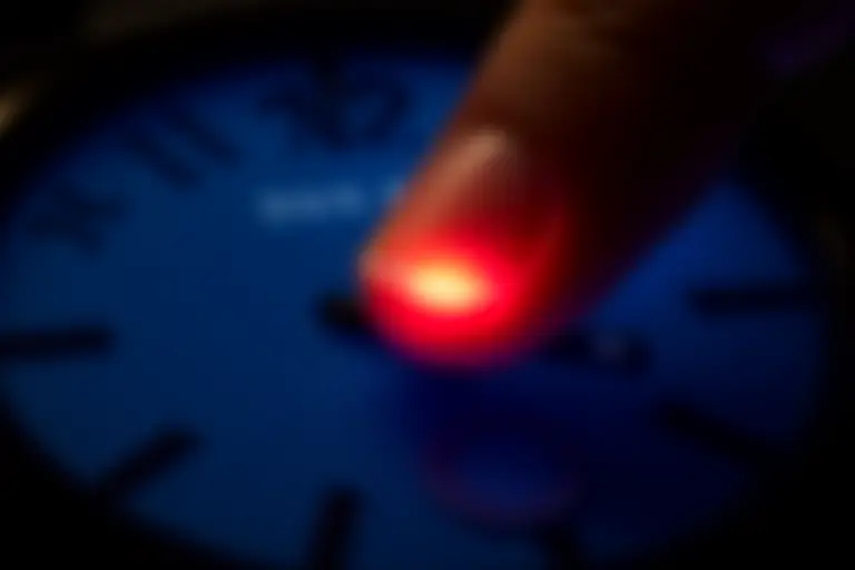 Close-up of a finger hovering over a small red button on a wristwatch