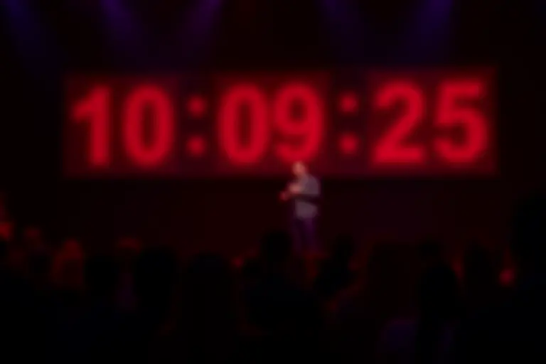 A stand-up comedian on stage with a large digital word counter ticking upward behind them